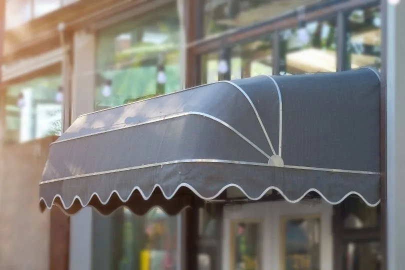 Toldo capota gris con faldón ondulado sobre el escaparate de un comercio