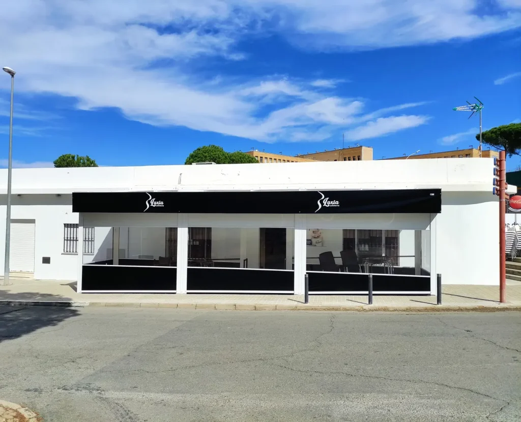 Cafetería con la terraza cerrada por cortavientos transparentes y faldón de lona negra